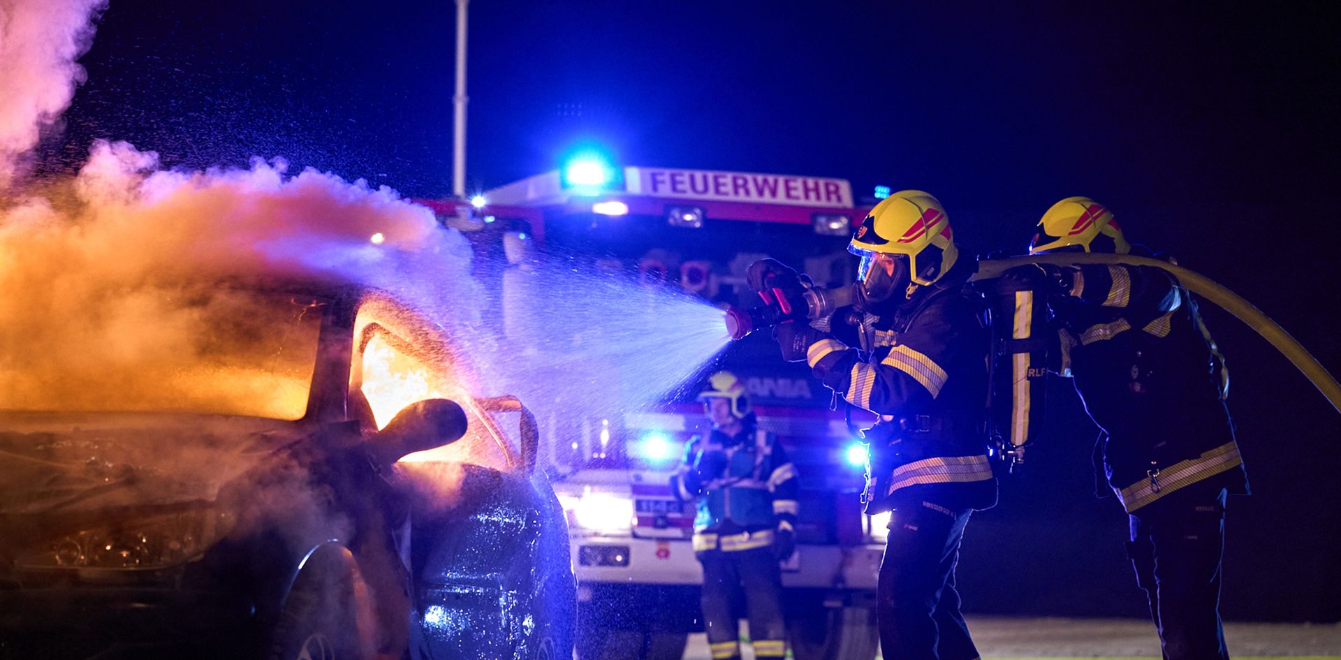 Feuerwehrleute der FF Gaaden unter Atemschutz löschen bei Nacht einen brennenden PKW, im Hintergrund das Einsatzfahrzeug mit Blaulicht